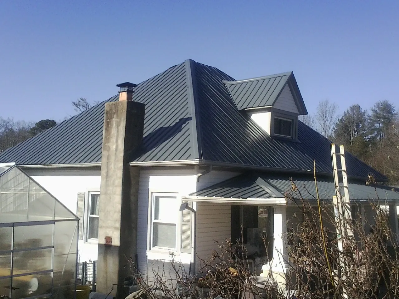 Dark blue standing seam metal roof on a white farmhouse with dormer — Slate & Tile Roof Repair by Roofing Brothers in Norris